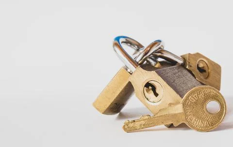 A closeup of a brass key in front of three interlinked padlocks on a white ba Stock Photos