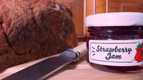 Closeup of bread, a knife and a small pot of strawberry jam. Stock Footage 297178455