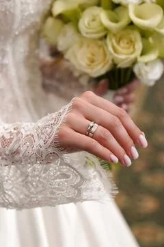 Closeup of the bride's hand with a wedding ring and white flower bouquet agai Stock Photos