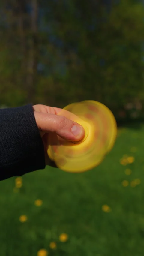 CloseUp of a Brightly Colored Fidget Spinner Held in Hand Against a Lush Green Stock Footage 308335349