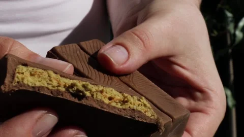 Closeup of broken dubai chocolate bar showing rich golden filling in hands under Stock Footage 310337706