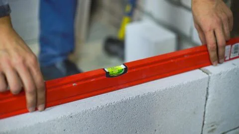 Closeup of builder checking evenness of aerated concrete wall with bubble level Stock Photos
