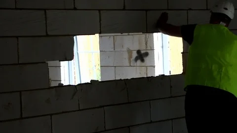 Closeup of a builder in high vis knocking breeze blocks out of a wall Stock Footage 112609464