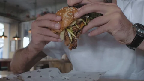Closeup burger with a duck in the hands of a man, then a man bites a burger Stock Footage 115634262