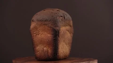 Closeup of burnt loaf of rye bread rotates on wooden board on brown background. Stock Footage 246217123