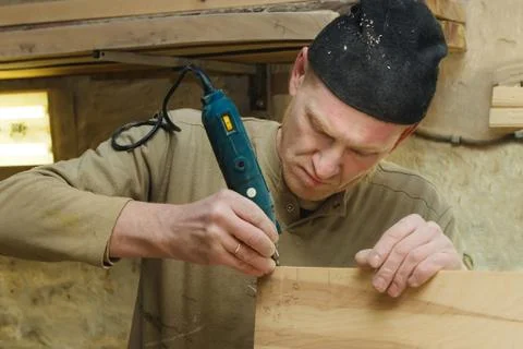 Closeup of Carpenter in Cap and Pullover Sanding Plank in Workshop. Industrial Stock Photos