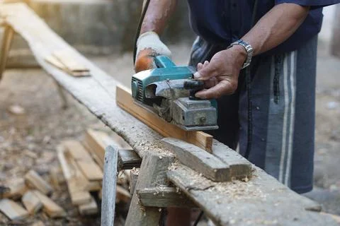 Closeup carpenter using electric planer with wooden plank in carpentry worksite. Stock Photos