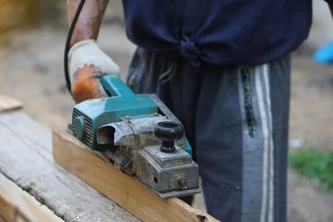 Closeup carpenter using electric planer with wooden plank in carpentry worksite. Stock Photos