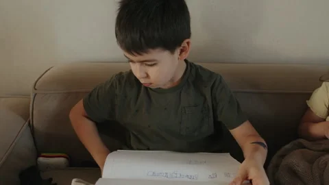 Closeup cheerful boy sitting on sofa writing using pencil sitting on sofa at Stock Footage 259231885