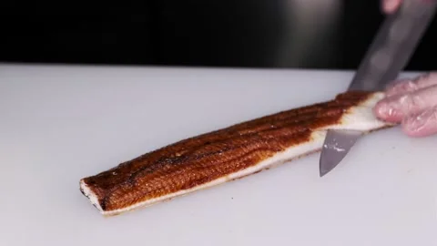 Closeup of the chef hands in gloves makes Japanese sushi rolls, cuts smoked eel Stock Footage 133654358