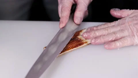 Closeup of the chef hands in gloves makes Japanese sushi rolls, cuts smoked eel Stock Footage 133654368