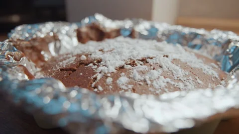 Closeup chocolate cake dusted sugar baking on foillined pan on kitchen counter Stock Footage 337460305