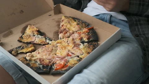 Closeup chopped pizza with black dough on man's knees in cardboard box. Stock Footage 152968752