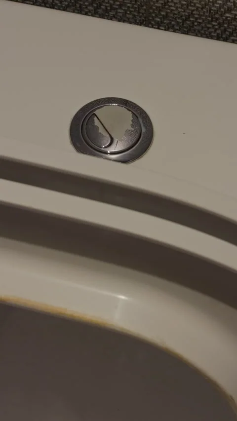 Closeup chrome flush button on toilet, subtle surface stains, textured lid edge Stock Footage 333907938