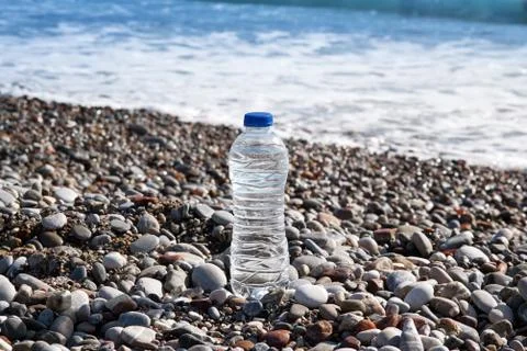 Closeup of Clear Plastic bottle with drinking water standing on the beach wit Stock Photos