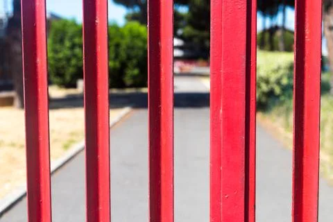Closeup of closed red gate. School park closed for visitors. Asphalt road and Stock Photos