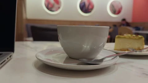 Closeup of coffee with blurred cake background. Portrait of latte on saucer with Stock Footage 333908438