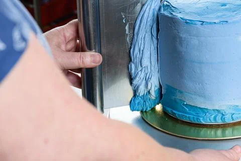 Closeup of a confectioner using a spatula on the side of the cake to spread t Stock Photos