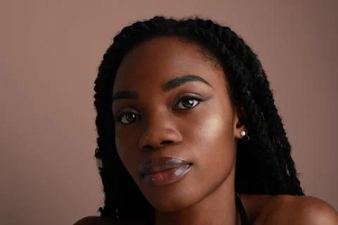 Closeup of a confident black African young woman with braids, beige background. Photos