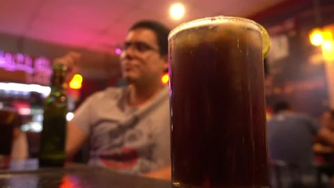 Closeup of a cuba libre on a bar table with a man in the background drinking bee Stock Footage 196736832