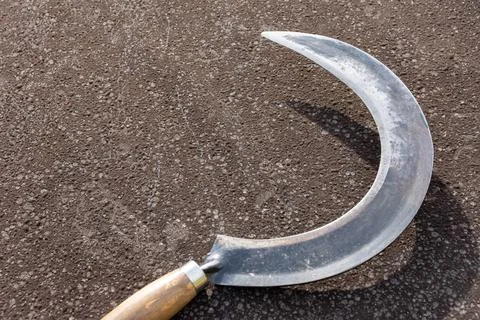 A closeup of a dangerously sharp sickle on the ground with its shadow visible Stock Photos