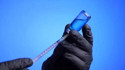 Closeup of doctor's hand in black gloves fill syringe on a blue background. Stock Footage 129706281