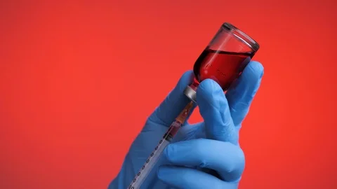 Closeup of doctor's hand in blue gloves fill syringe on a red background. Stock Footage 129095934