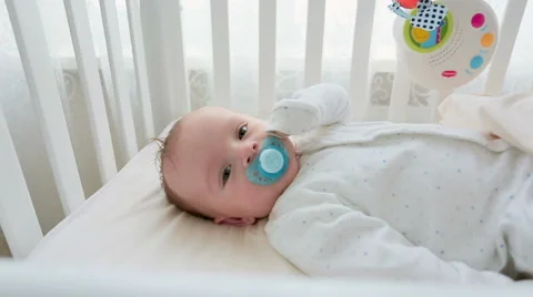 Closeup dolly shot of cute 3 months old baby boy lying in bed with toy carous Stock Footage