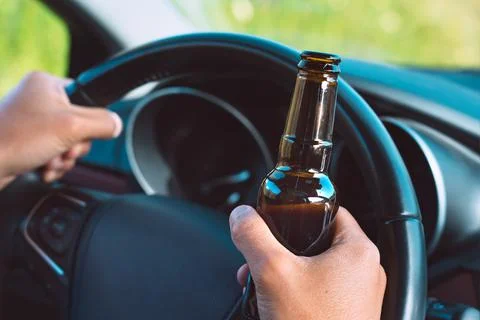 Closeup of drunk driver hands on the steering wheel with a bottle of beer Stock Photos