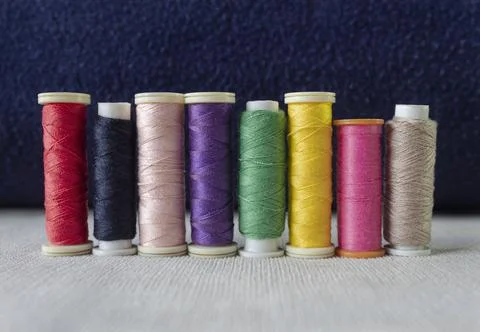 Closeup to a eight multicolor sewing threads over white textile Stock Photos