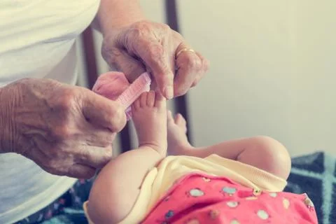 Closeup of elderly hands putting socks on newborn feet. Stock Photos