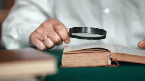 Closeup elderly man hands reading old retro text book use magnifying glass Video stock 165036156