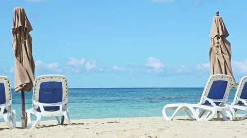 Closeup empty golden sandy ocean shore with beach chairs and closed umbrellas Video stock 129777739