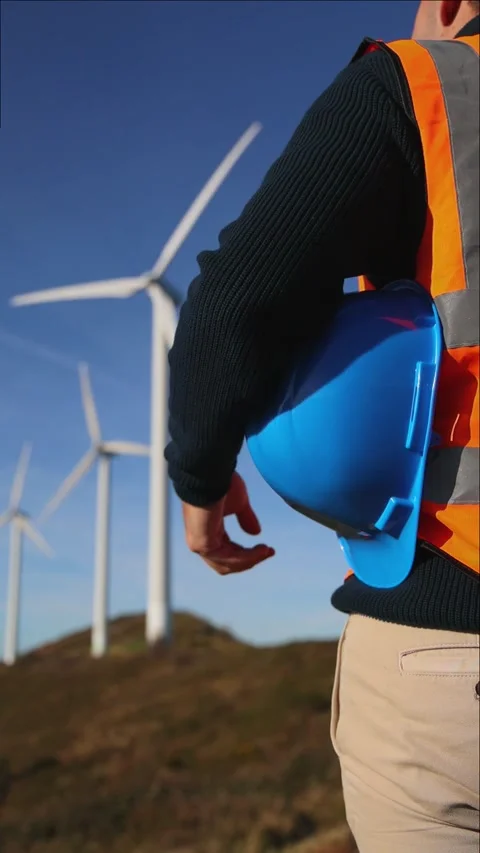 Closeup of engineer standing towards wind turbines holding helmet Stock Footage 294976140