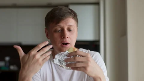 Closeup face of hungry young man eating delicious spicy sandwich, airing out Vidéo 251587695