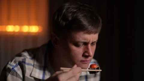 Closeup face of young hungry man sniffs spoiled seafood in sushi snacks, eating Stock Footage 266123189