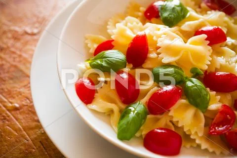 Closeup Of Farfalle Pasta Cherry Tomatoes And Basil Over A Colored Background