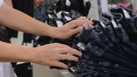 Closeup female hands sorting through stack of folded fashionable jeans. Person Stock Footage 257324860