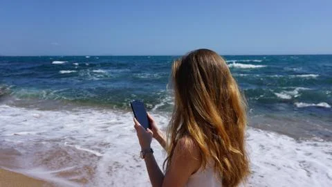 Closeup of a female using mobile phone, beach and sea on background Stock Photos