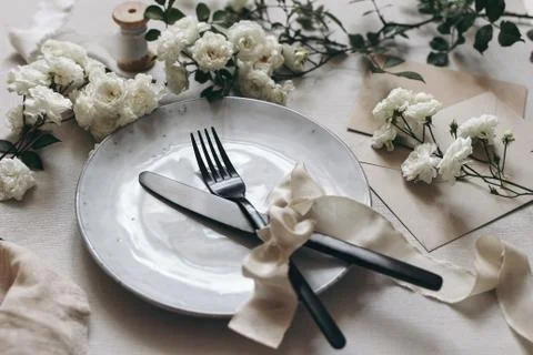 Closeup of festive table setting with black cutlery, white rose flowers, silk Fotos Stock