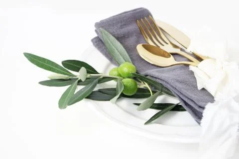 Closeup of festive table summer setting with golden cutlery, olive branch, grey Foto stock