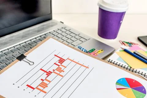 Closeup of a financial data chart, laptop and note pads on an office desk Stock Photos