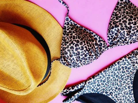 Closeup of a flat lay with leopard bikini and a straw hat on pink background Stock Photos