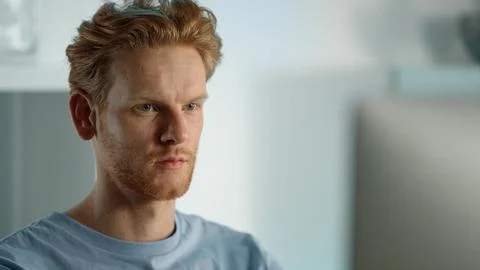 Closeup focused developer working at home office. Serious ginger man browsing Stock Photos