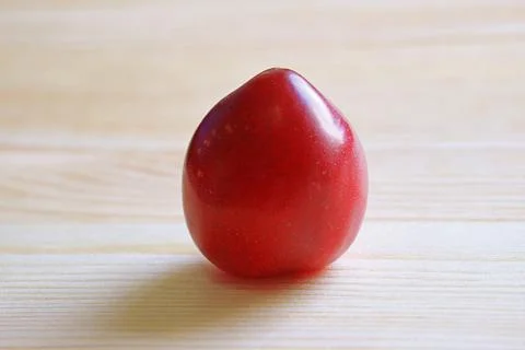 Closeup of a Fresh Dwarf Gulf Ruby Plum Isolated on Wooden Background Foto stock