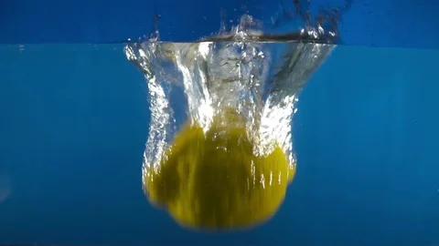 Closeup of fresh lemon falling into water on the blue background slow motion Video stock 75787259
