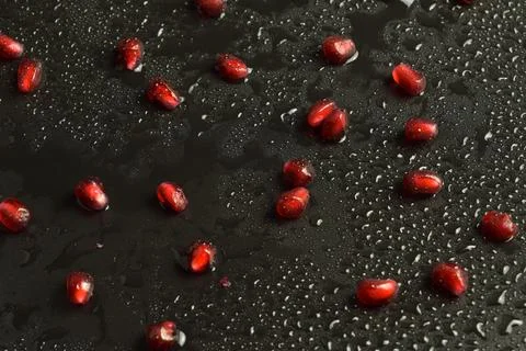 Closeup fresh pomegranate arils on black background water droplets Stock Photos