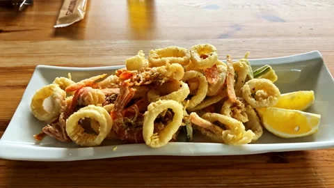 Closeup of Fried Calamari Plated With Lemon Wedges in a Restaurant Stock Footage 328948906