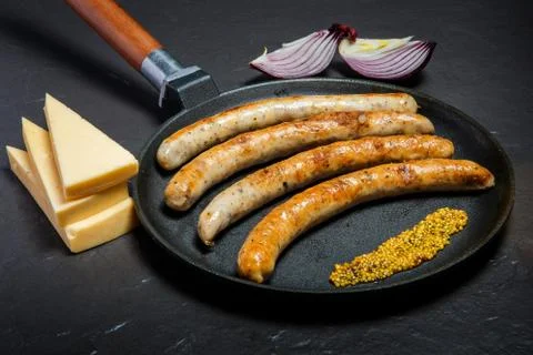 Closeup frying pan with fried thin sausages and granular mustard Fotos de archivo