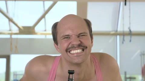 Closeup, funny bald man is training on an exercise bike, smiling Stock Footage 130899896